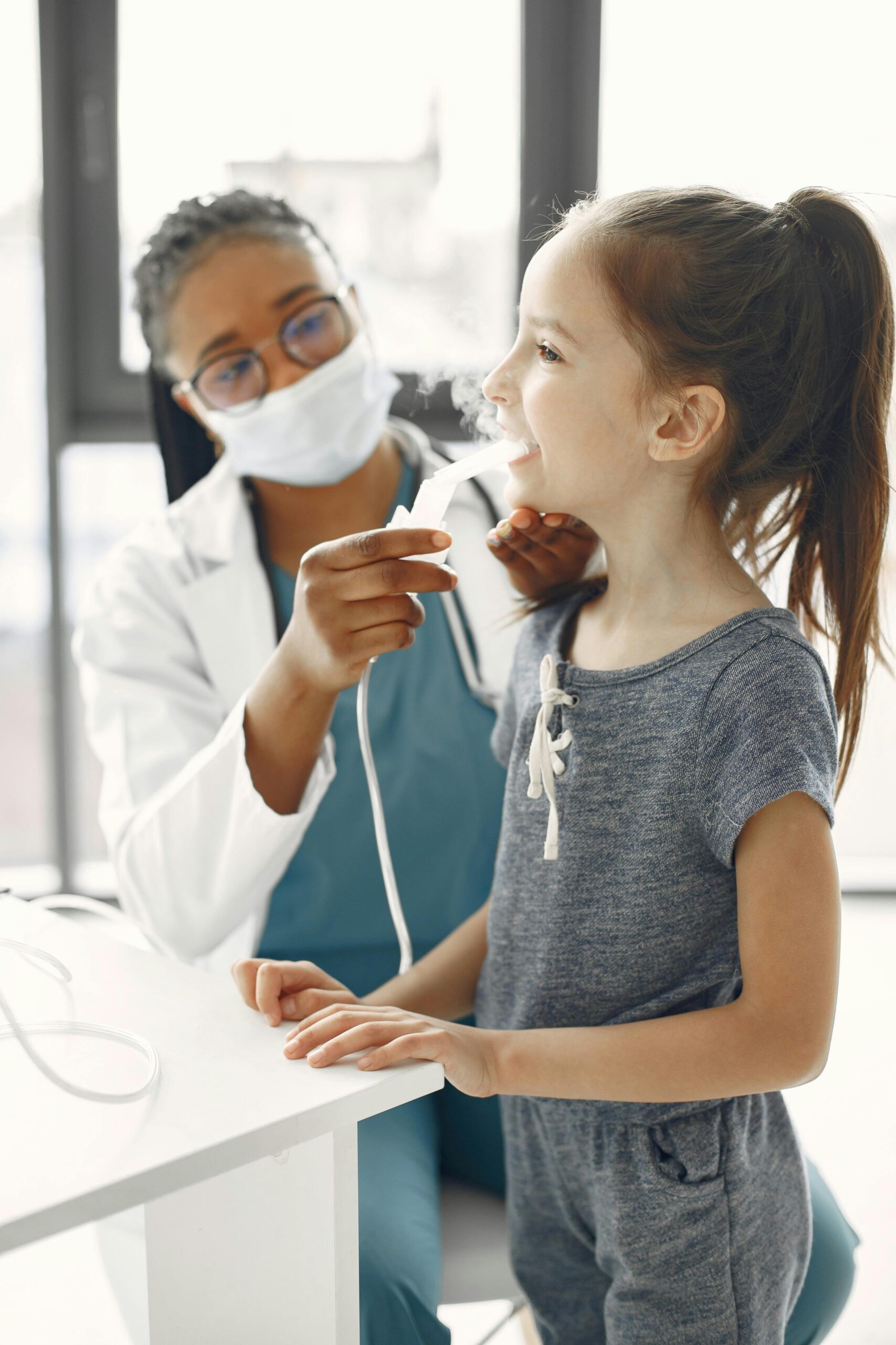 A doctor provides nebulizer treatment to a smiling child in a clinic setting. Health and care concept.